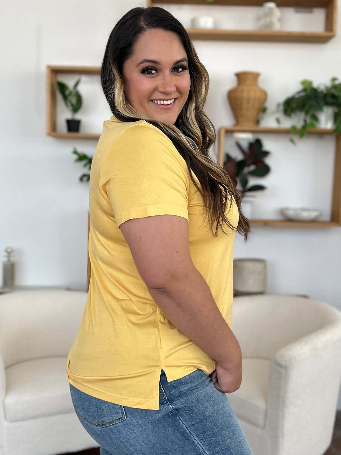 Woman wearing a yellow Bamboo V-Neck High-Low T-Shirt, showcasing side view with slight stretch and comfortable fit.