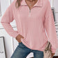 Woman wearing a pink striped half zip long sleeve t-shirt with jeans, holding a beige handbag.