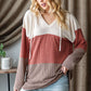 Woman wearing Color Block Long Sleeve Hoodie with trendy design and ripped jeans, standing indoors against a curtain background.