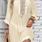 Woman wearing a beige sheer fringe tie neck three-quarter sleeve cover-up with embroidered detailing, holding a woven bag.