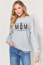 Woman wearing a grey long sleeve sweatshirt with "MOM mode" graphic, paired with blue jeans.