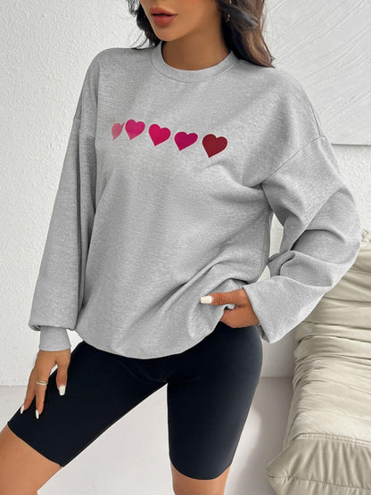 Woman wearing Devine Heart Dropped Shoulder Long Sleeve Sweatshirt in gray with heart patterns, paired with black shorts.