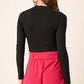 Back view of a woman in a black long sleeve crop knit top paired with stylish pink shorts.