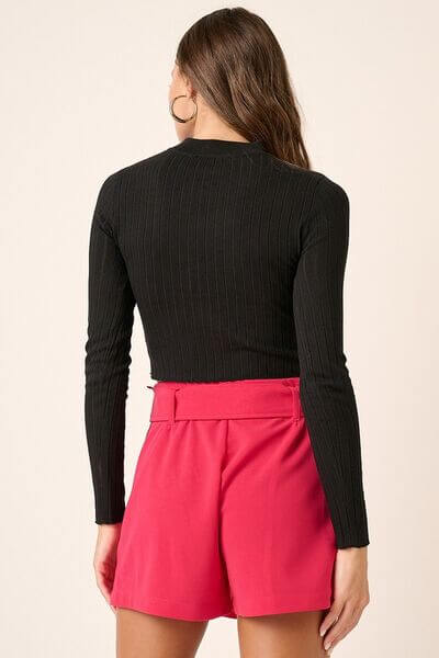 Back view of a woman in a black long sleeve crop knit top paired with stylish pink shorts.