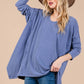 Woman wearing Ces Femme asymmetrical long sleeve top with relaxed fit, soft knit fabric, and hi-low hem, styled with a hat.