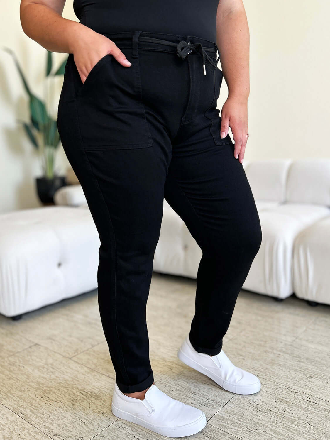 Woman wearing high waist black skinny jeans with a tie waist bow and white slip-on shoes