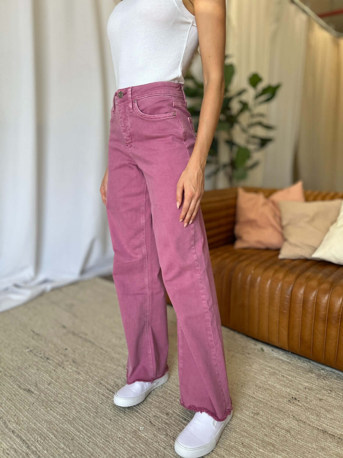 Woman wearing pink high rise wide leg jeans with white tank top and sneakers in a stylish indoor setting