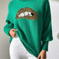 Green Bella Road Lip Turtleneck Sweater with bold lip design, long sleeves, modeled with white pants, quirky and stylish statement piece.