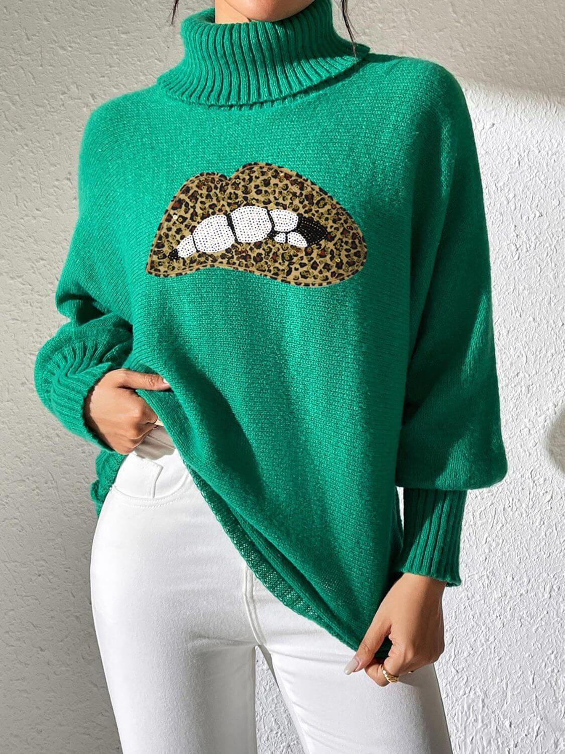 Green Bella Road Lip Turtleneck Sweater with bold lip design, long sleeves, modeled with white pants, quirky and stylish statement piece.