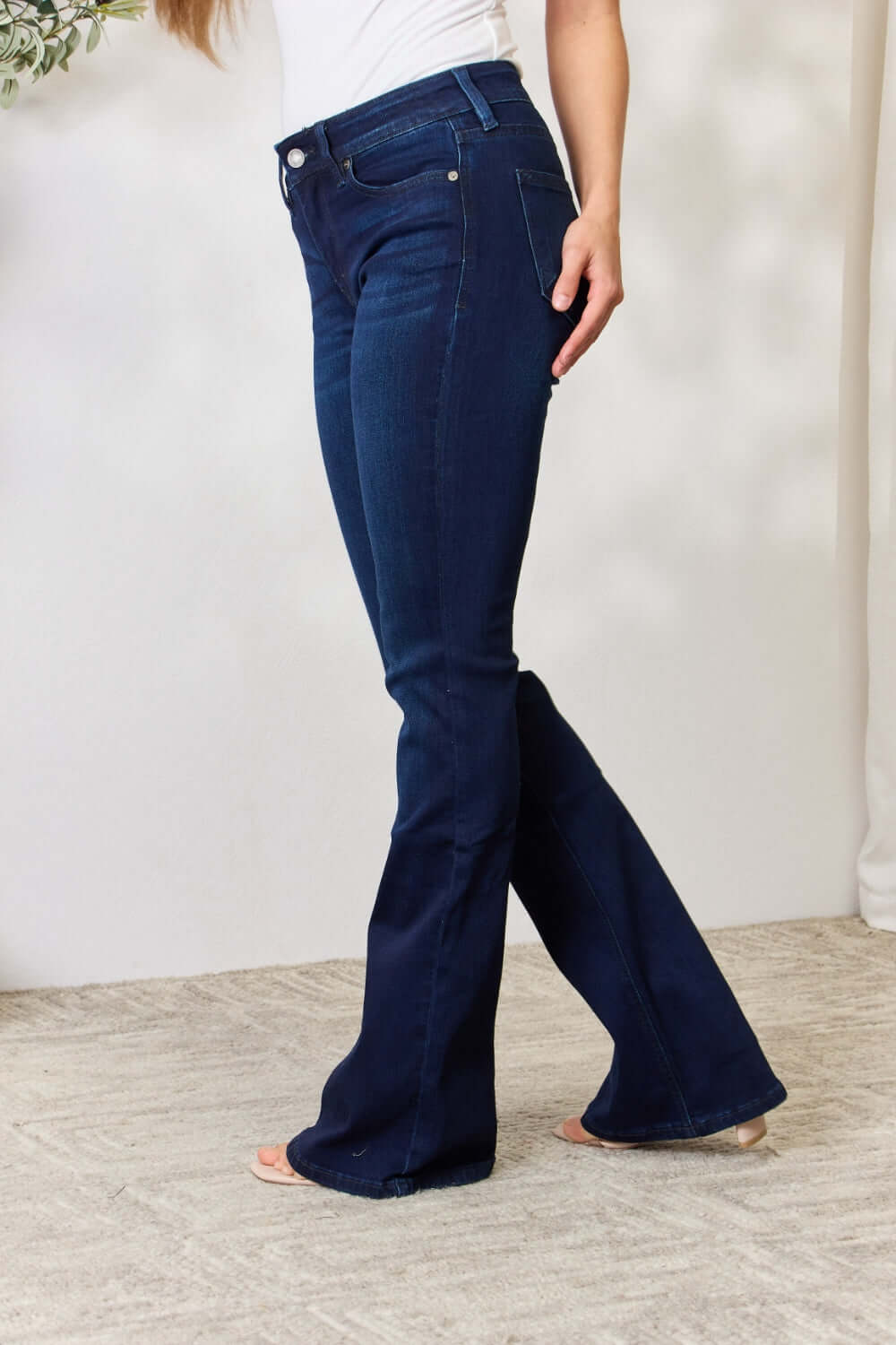 Woman wearing mid rise flare jeans in dark denim with a clean, non-distressed look, highlighting a timeless silhouette with a comfortable fit.