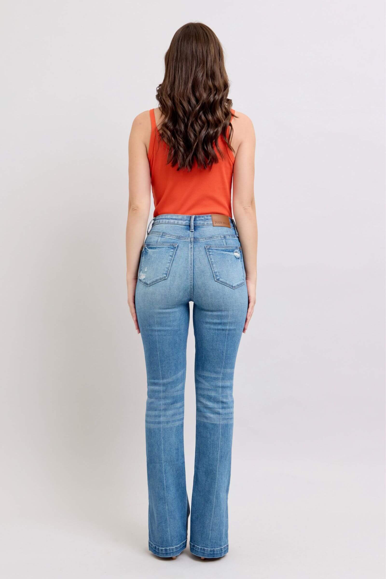 Back view of woman in Judy Blue high waist vintage wash bootcut jeans with side slits, styled with a red tank top.