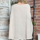 Woman wearing Bella Road Round Neck Batwing Sleeve Sweater in cream color, standing near a rustic brick wall.