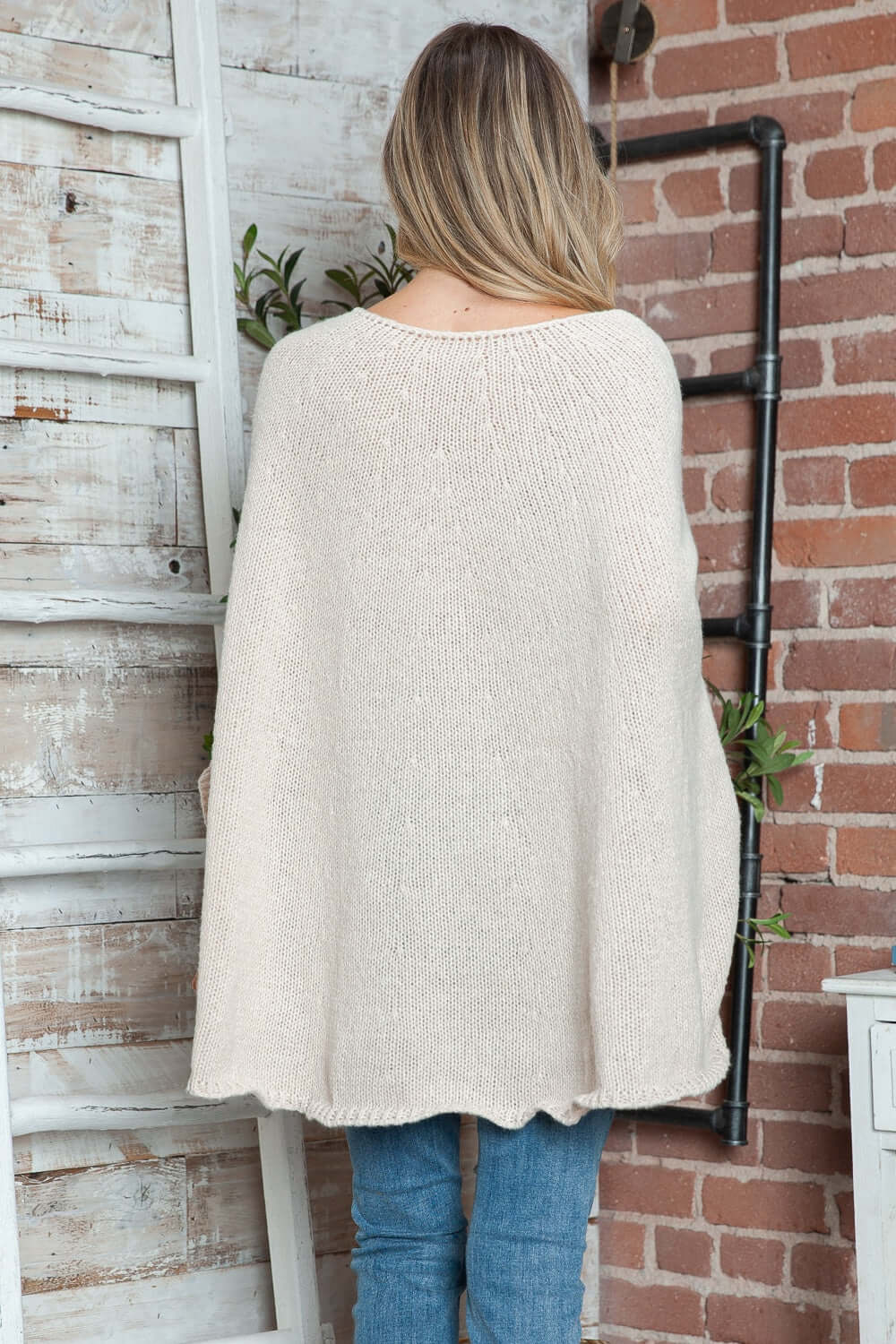 Woman wearing Bella Road Round Neck Batwing Sleeve Sweater in cream color, standing near a rustic brick wall.