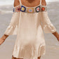 Woman wearing a crochet cold shoulder three-quarter sleeve cover up on a beach with ruffled hem and colorful floral detailing.