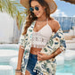 Woman in floral print tassel cover-up and wide-brimmed hat, enjoying a sunny beach day by the pool.