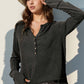 Woman wearing Double Take Full Size Notched Thumbhole Long Sleeve T-Shirt in dark color with a hat and white jeans.