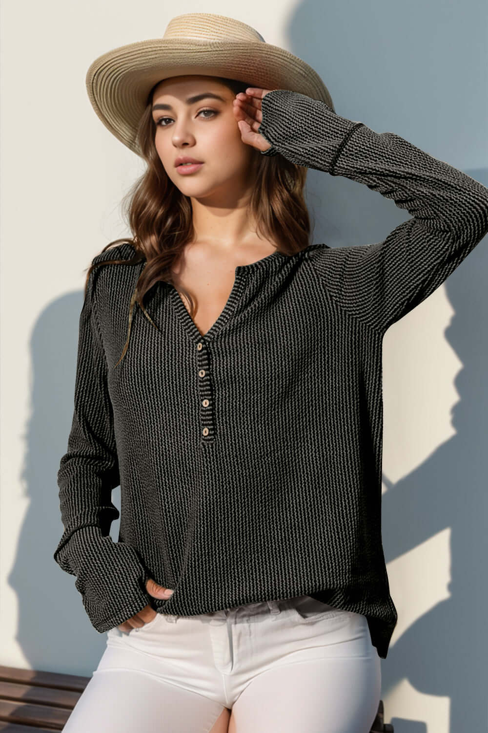 Woman wearing Double Take Full Size Notched Thumbhole Long Sleeve T-Shirt in dark color with a hat and white jeans.