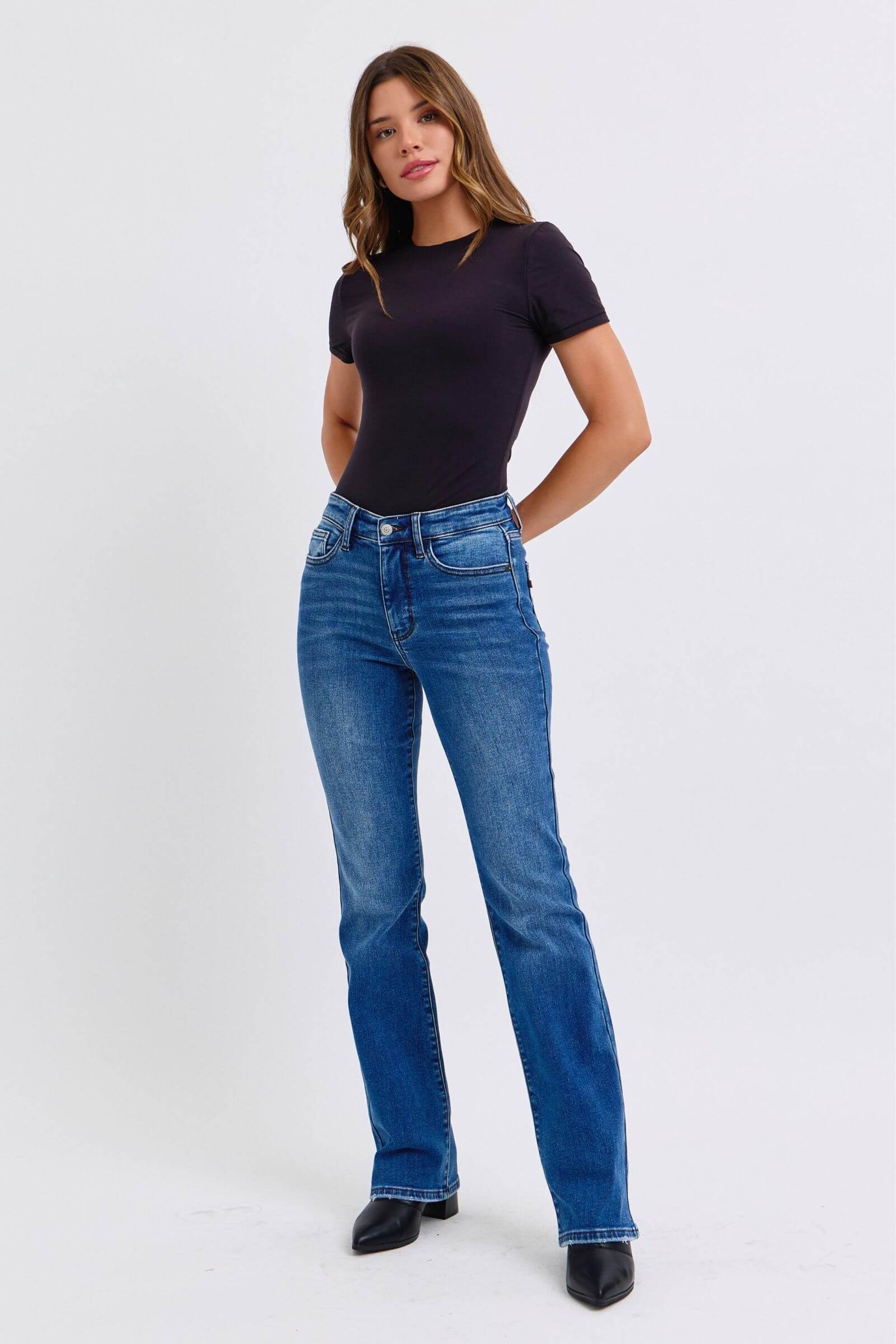 Model showcasing Judy Blue Mid-Rise Bootcut Jeans with thermal lining in a stylish, casual outfit.