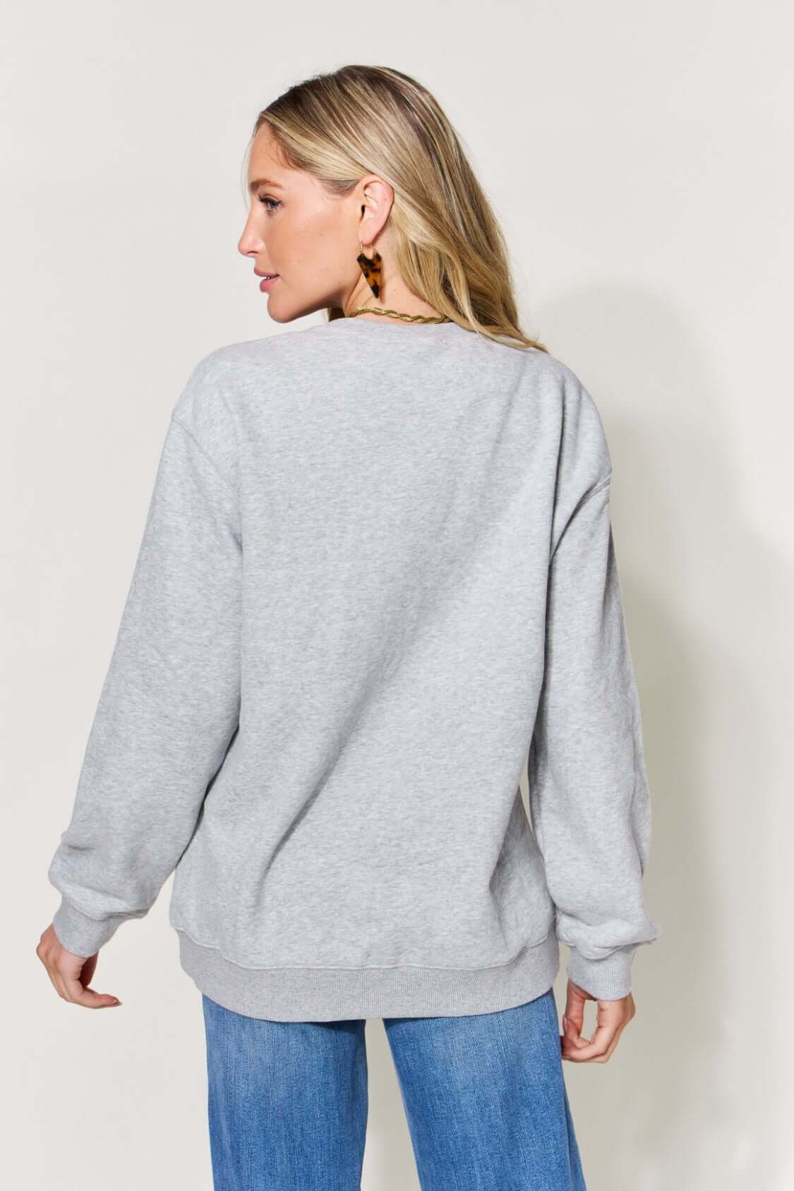 Woman wearing grey letter graphic long sleeve sweatshirt in full size, showing back view.