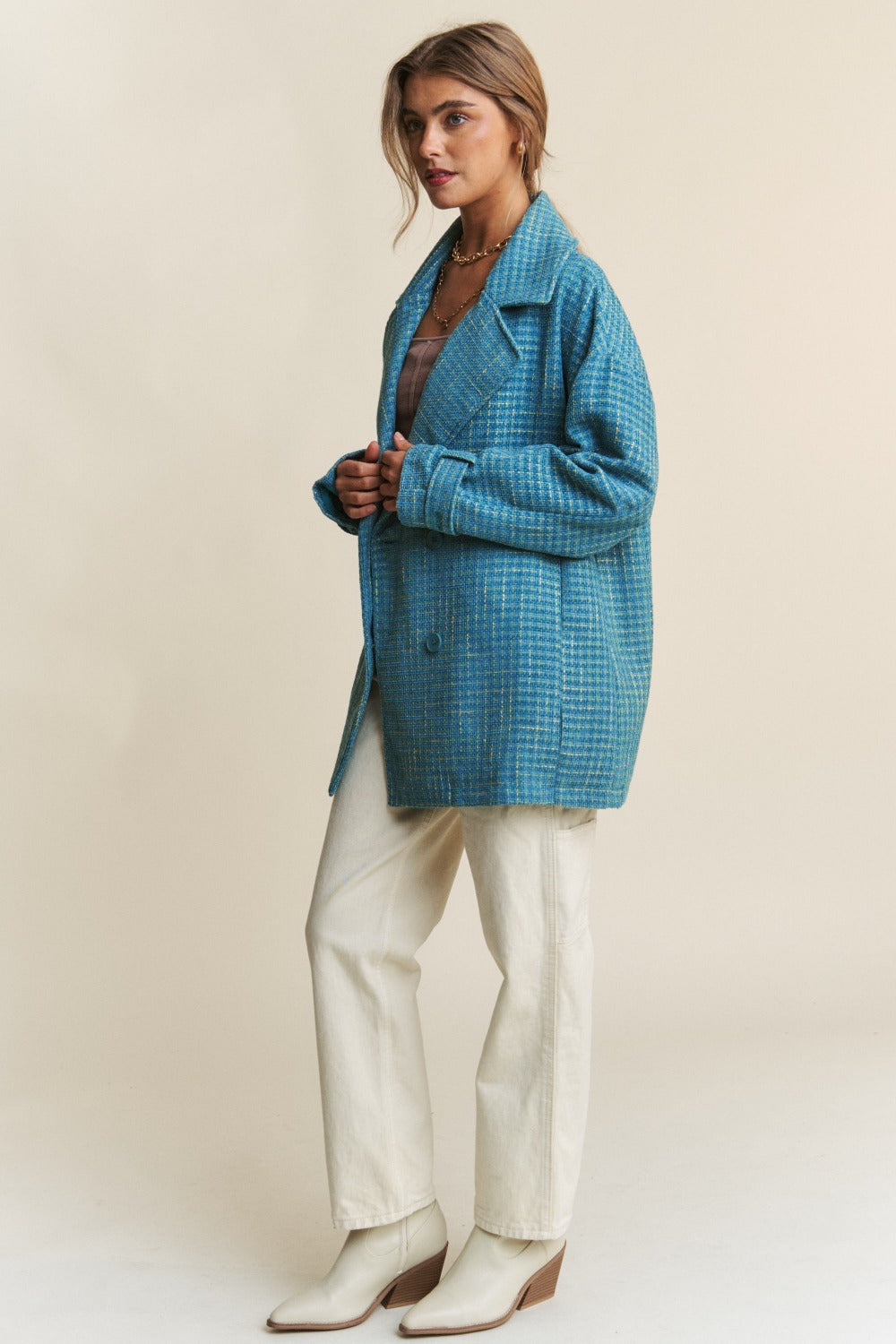 Woman wearing a blue tweed double-breasted coat with long sleeves, styled with white pants and heeled boots, showcasing sophisticated fashion