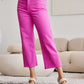 Woman wearing Tummy Control High Waist Raw Hem pink jeans from RFM Jeans, standing in a stylish living room environment