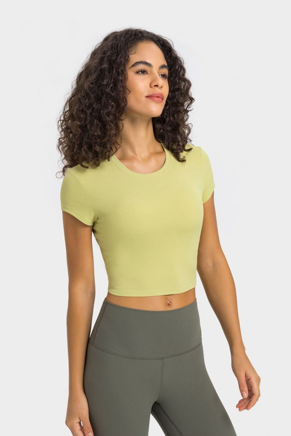 Woman in a cropped round neck short sleeve sports t-shirt, perfect for yoga, styled in soft lime green with leggings.