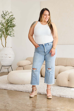 Woman wearing Tummy Control High Waist Raw Hem Distressed Jeans by RFM Jeans in a stylish living room.