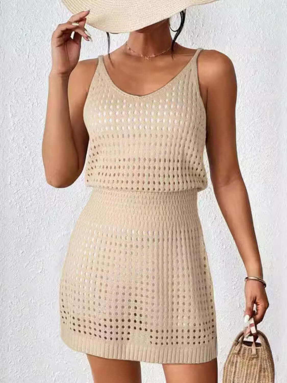 Beige openwork V-neck sleeveless cover-up dress, perfect for summer; made of stretchy, sheer 100% acrylic material. Model holding hat.