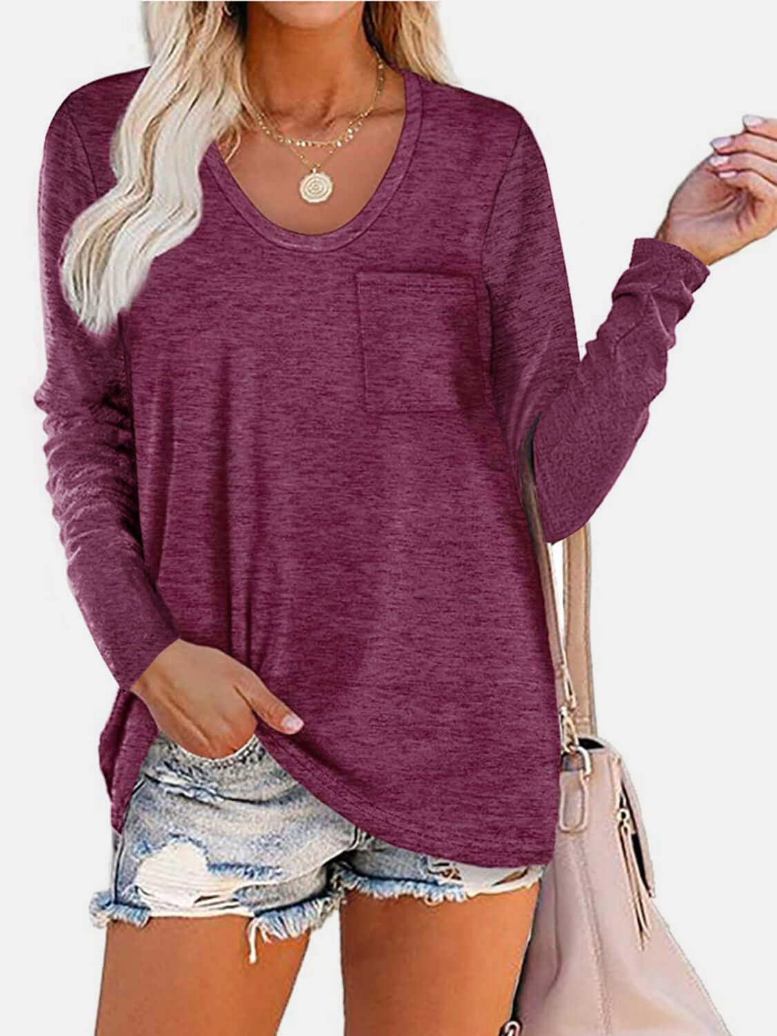 Woman wearing Bella Road round neck long sleeve T-shirt in burgundy with front pocket, paired with denim shorts and beige handbag.