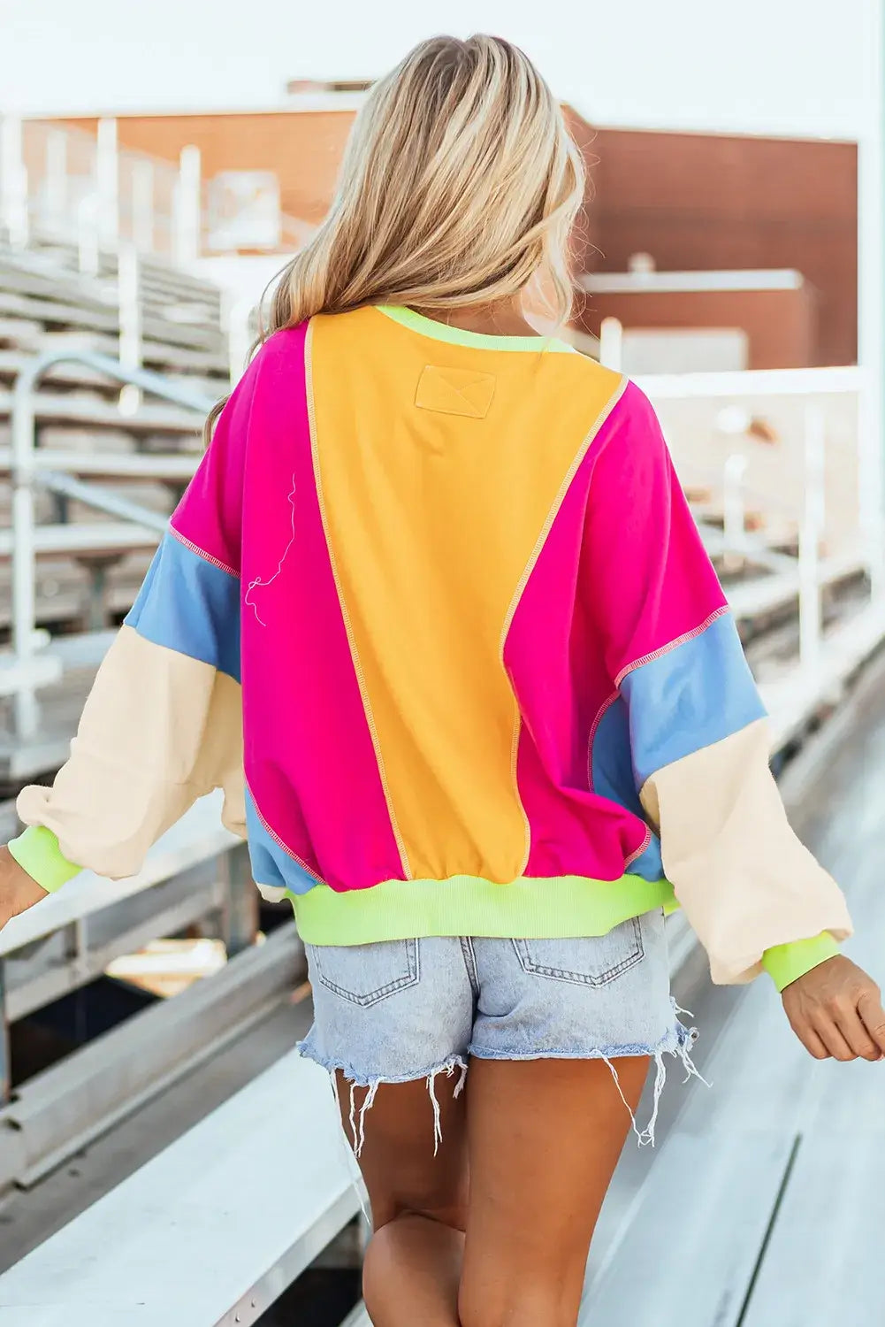 Woman wearing Bella Road Color Block Round Neck Long Sleeve Top, outdoors, displaying trendy vibrant design with casual shorts