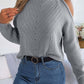 Stylish woman in gray cable-knit turtleneck cold shoulder sweater and jeans, showcasing cozy yet trendy fashion.