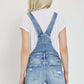 Back view of Risen Jeans distressed raw hem denim overalls, showcasing trendy raw hem and distressed detailing.