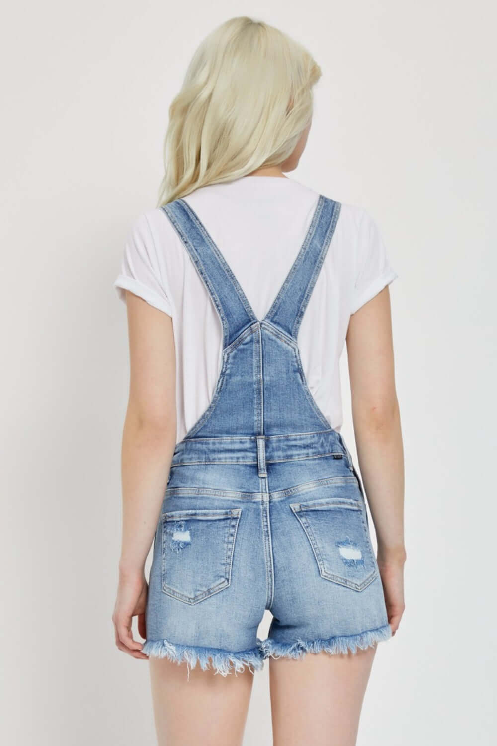 Back view of Risen Jeans distressed raw hem denim overalls, showcasing trendy raw hem and distressed detailing.