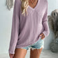 Woman wearing Double Take Pocketed Textured V-Neck Long Sleeve T-Shirt in light purple paired with distressed denim shorts.