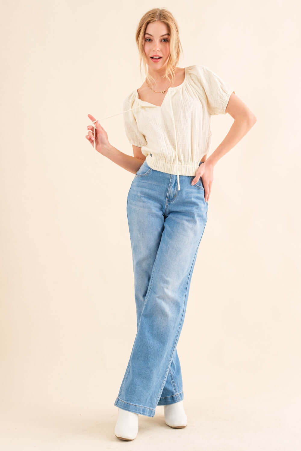 Woman wearing Back Waist Tie Cropped Blouse paired with high-waisted blue jeans and white ankle boots.