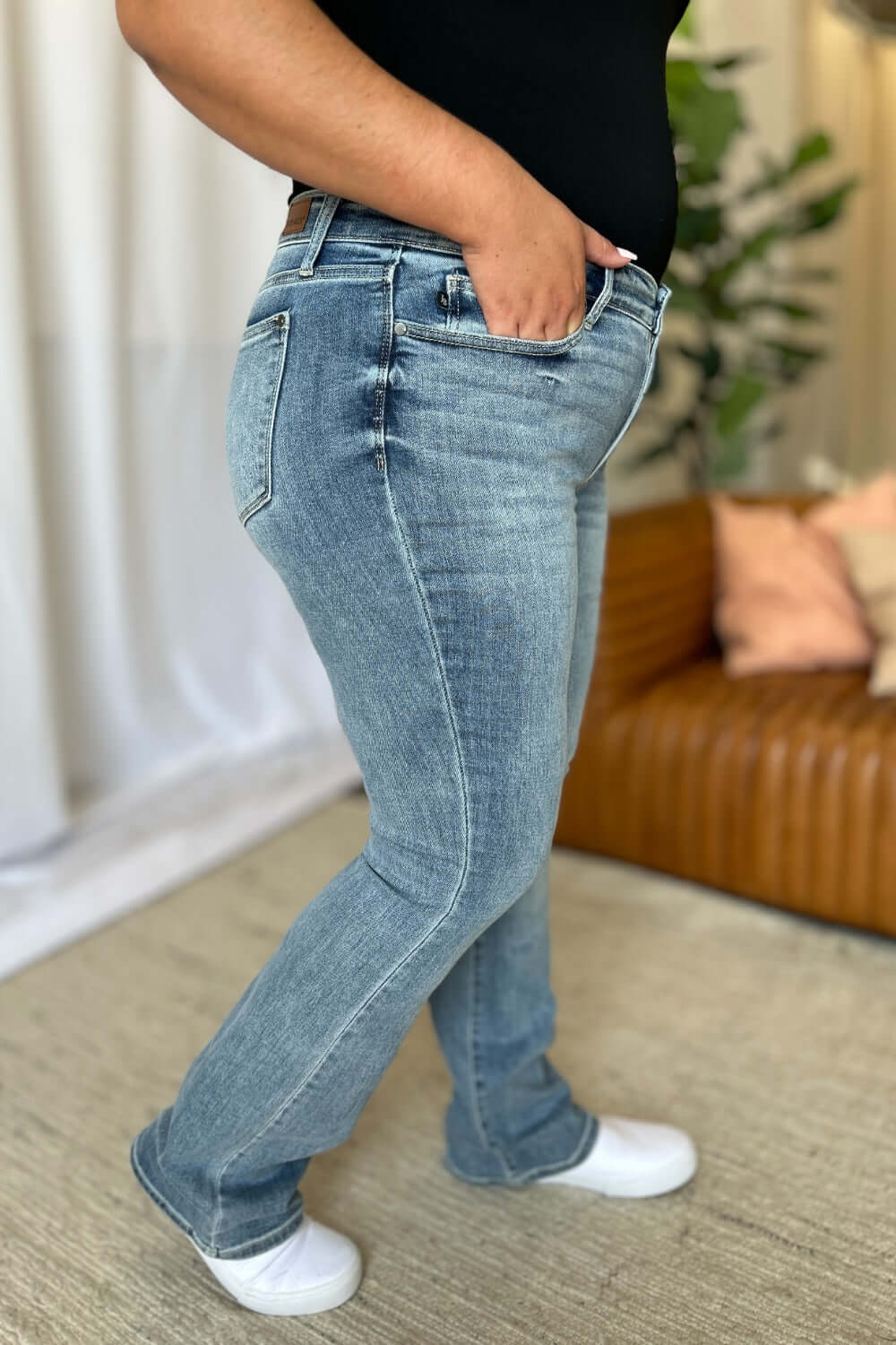 Woman wearing Judy Blue full size medium rise bootcut jeans with a casual fit, standing in a cozy living room.