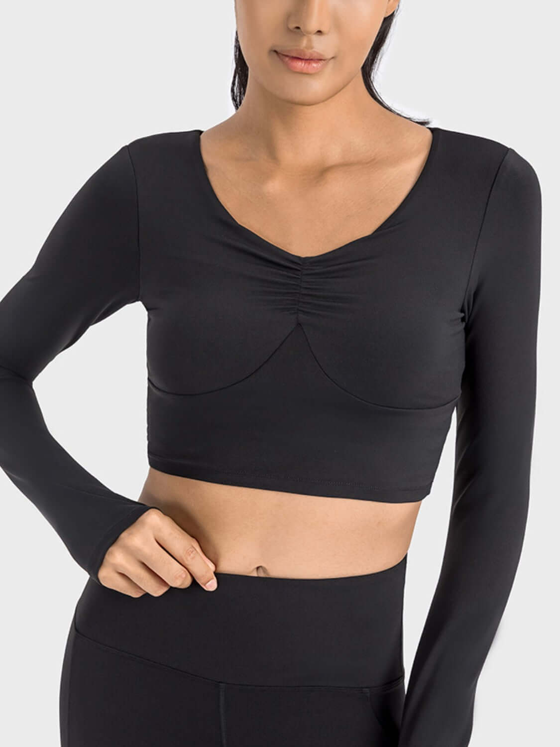 Model wearing the Millennia Ruched Cropped Long Sleeve Sports Top in black, showcasing its stylish design and fitted silhouette.