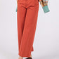 Woman wearing wide leg cropped pants with a front pocket and button closure, styled with sandals and an orange cardigan.