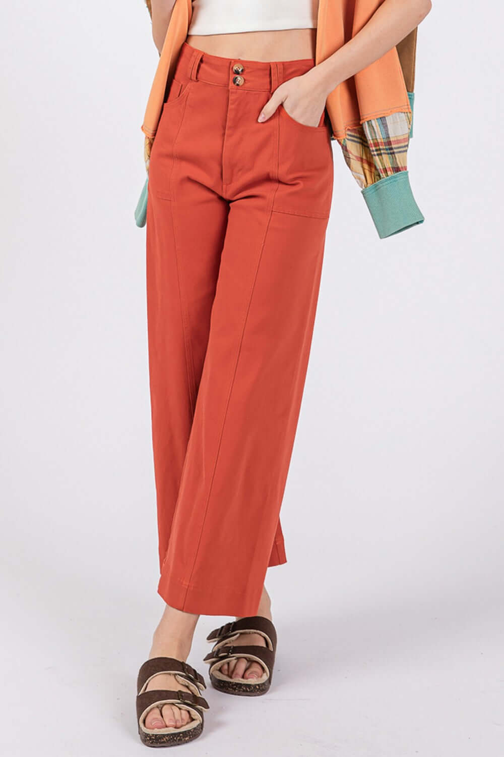 Woman wearing wide leg cropped pants with a front pocket and button closure, styled with sandals and an orange cardigan.