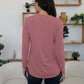 Woman in dusty pink FAM-FAM round neck long sleeve t-shirt, standing in stylish room, showcasing comfortable casual wear.