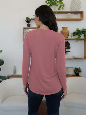 Woman in dusty pink FAM-FAM round neck long sleeve t-shirt, standing in stylish room, showcasing comfortable casual wear.