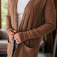 Woman wearing a textured open front cover up with pockets in brown, paired with a white top.