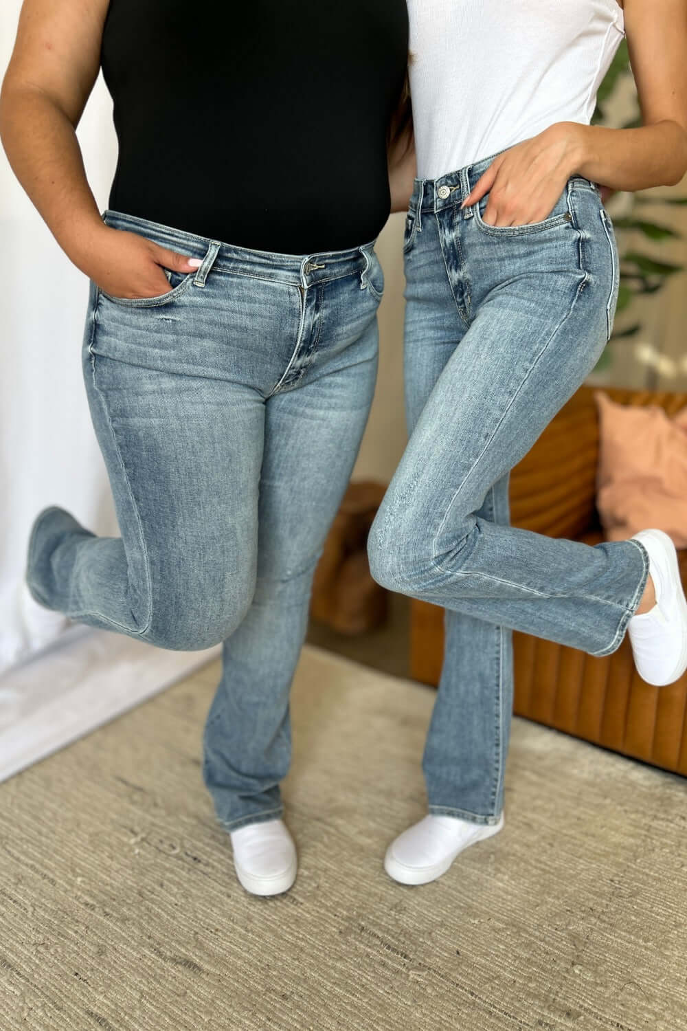 Two people wearing Judy Blue full size medium rise bootcut jeans, demonstrating a comfortable and stylish fit for all body types.