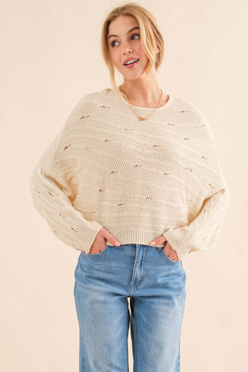 Woman wearing a cozy Dolman Sleeves Sweater in cream with blue jeans, showcasing its relaxed fit and trendy, versatile design.