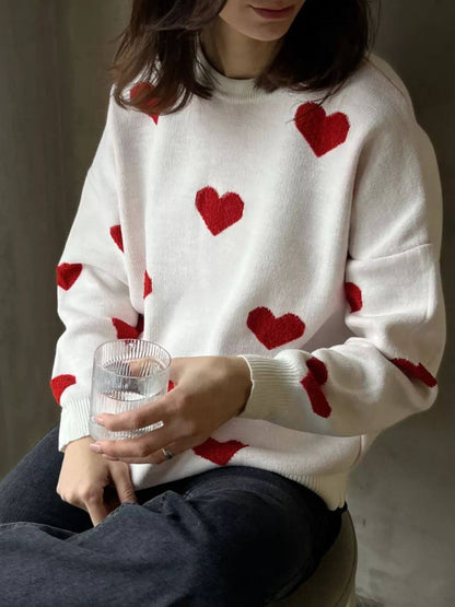 Woman wearing Bella Road Heart Round Neck Dropped Shoulder Sweater with red heart detailing, holding a glass.