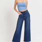 Model wearing high rise raw hem cropped wide leg jeans from Risen Jeans with a blue tank top and black heels