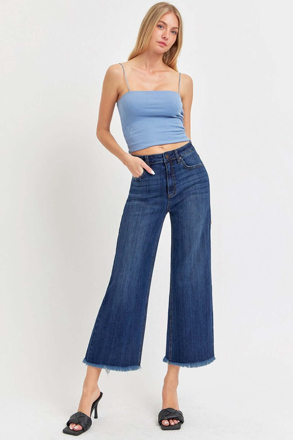 Model wearing high rise raw hem cropped wide leg jeans from Risen Jeans with a blue tank top and black heels