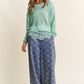 Woman wearing J.NNA lace detail long sleeve knit top in green with wide-legged patterned pants.