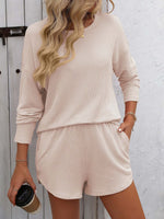 Woman wearing Double Take round neck long sleeve top and shorts set in beige, holding a coffee cup, featuring pockets and a trendy style.