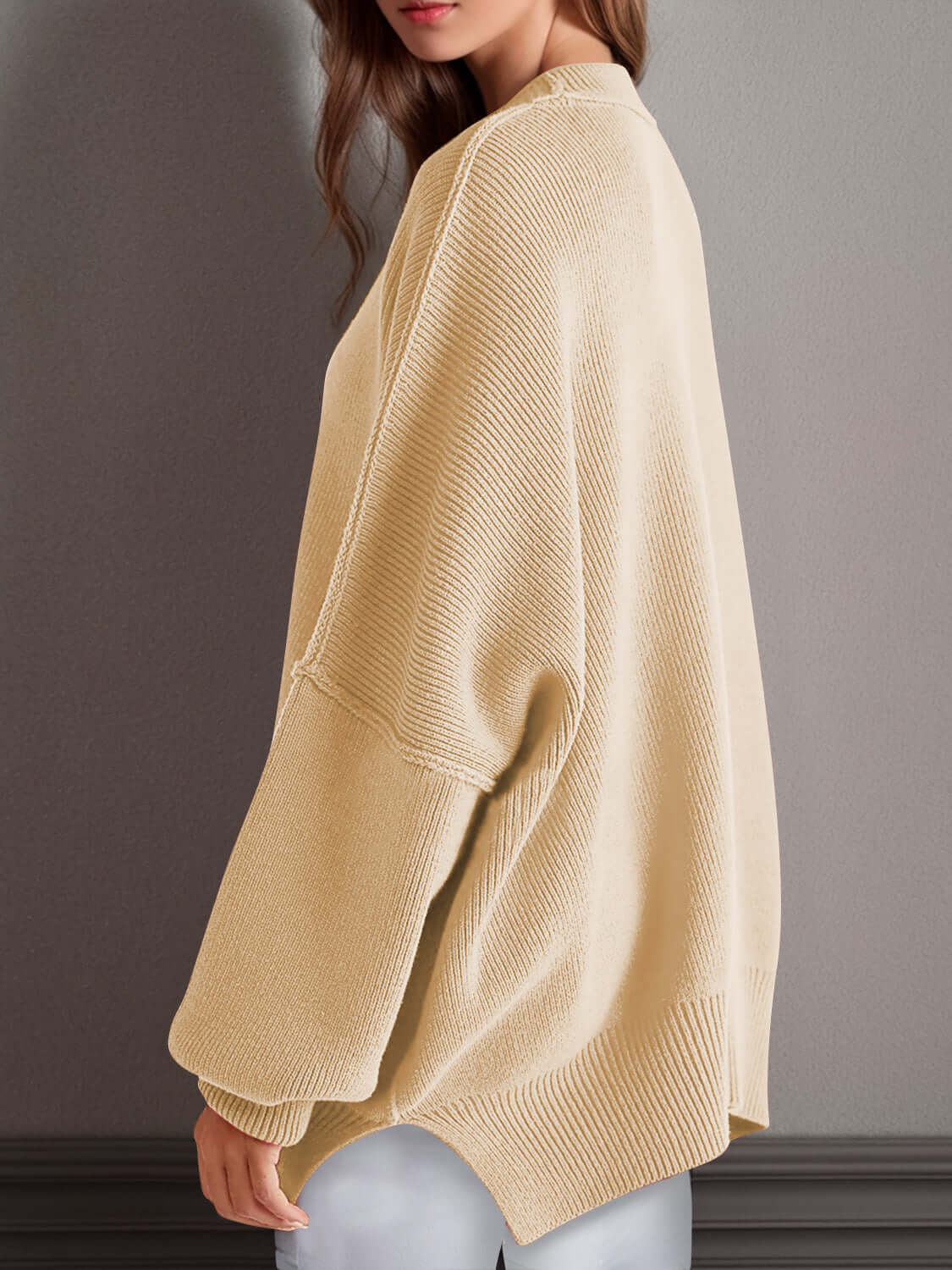 Woman wearing a cozy double take side slit round neck long sleeve sweater in beige, showcasing back side split detail.